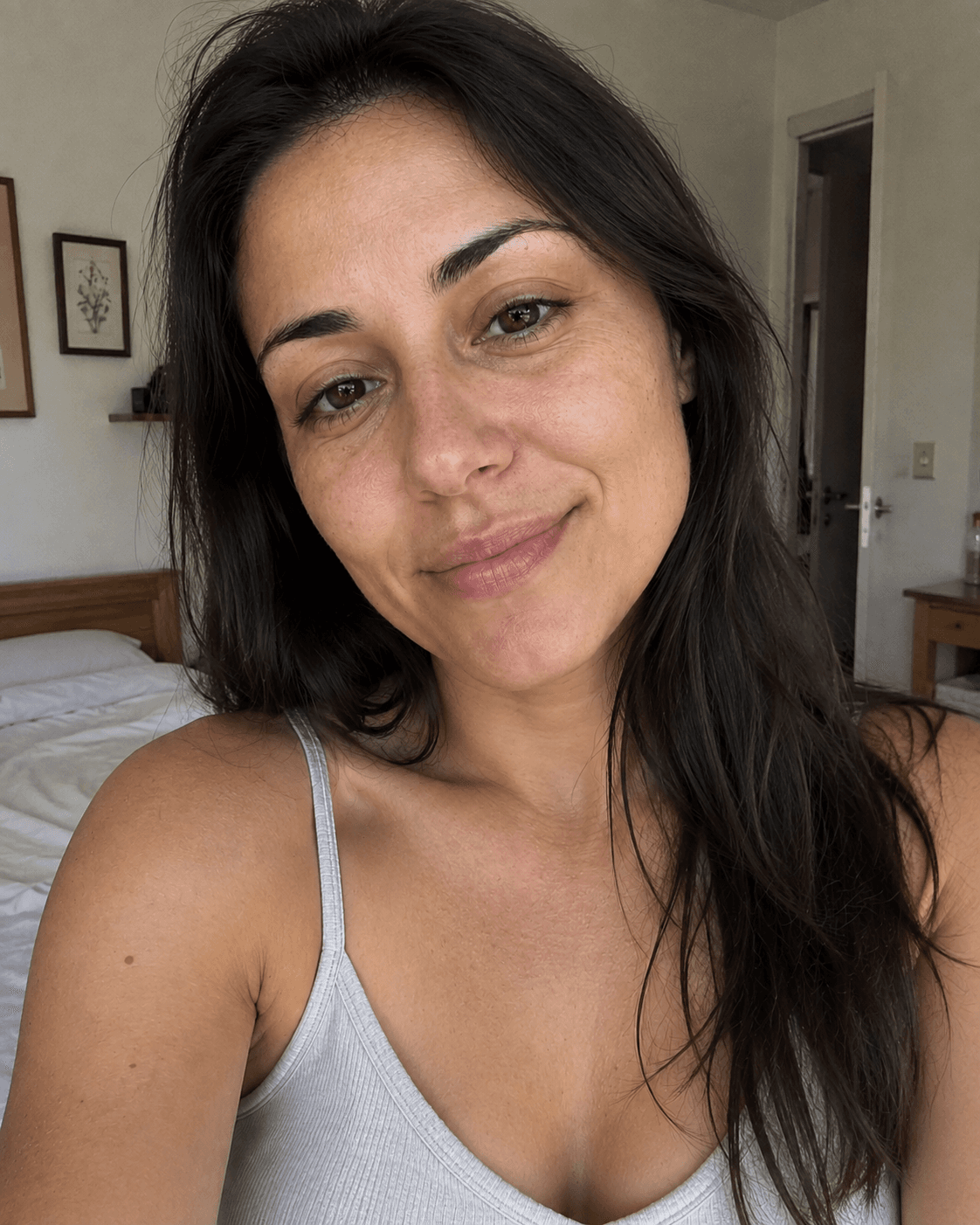 Donna con lunghi capelli scuri sorride dolcemente in un selfie ravvicinato in una stanza luminosa.